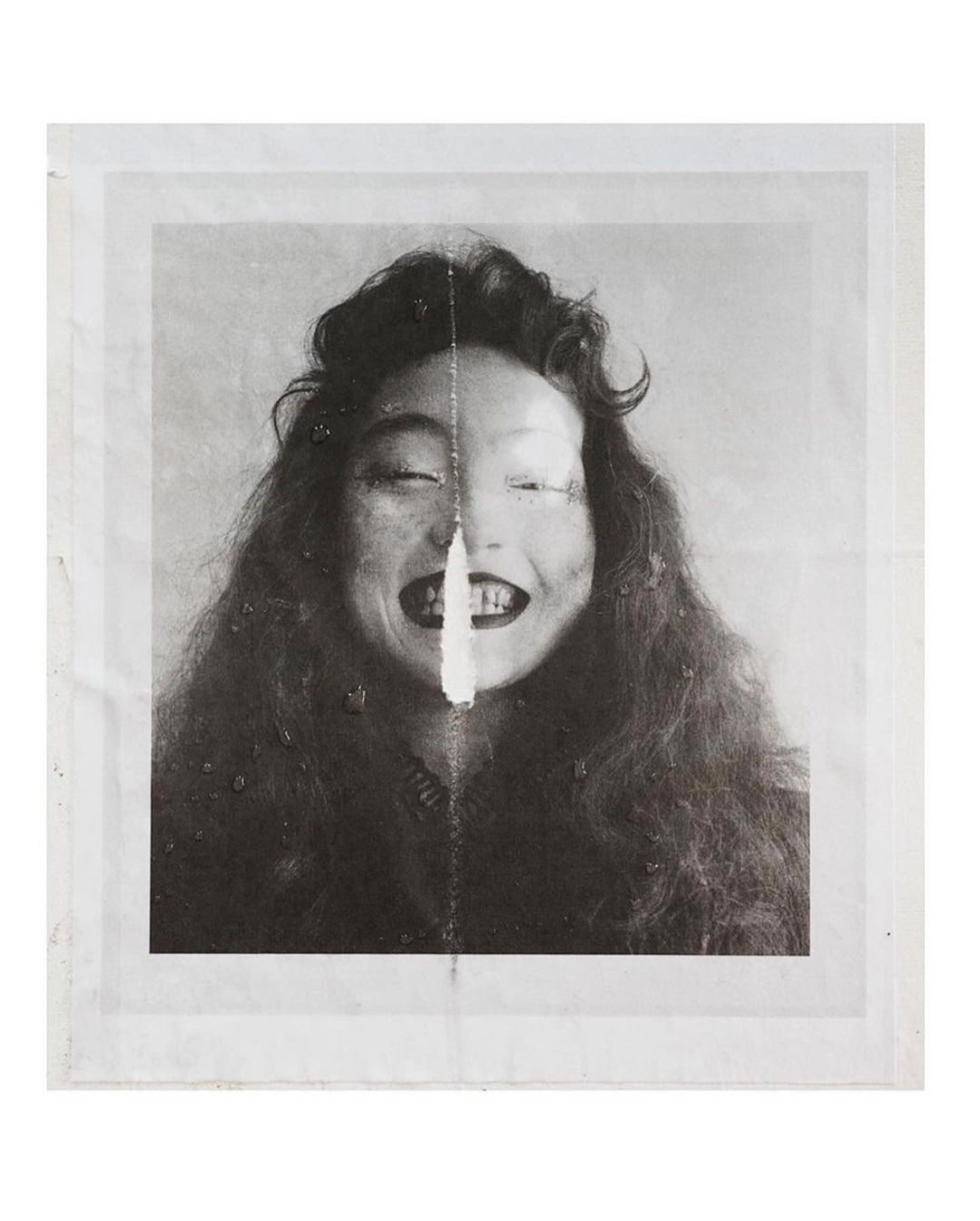 Portrait of a young woman with curly hair smiling and eyes closed in a black and white photo, presented in a plastic sleeve.