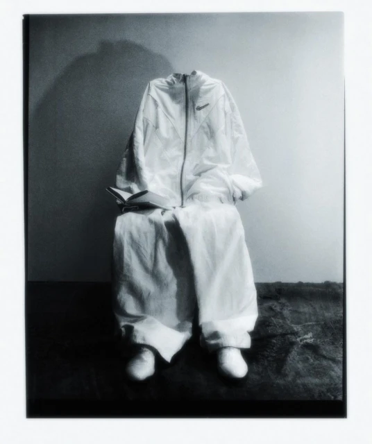 White athletic suit and shoes arranged on a chair against a two-tone background. The book adds a literary touch.