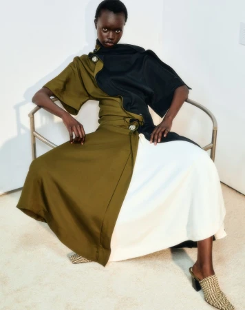 Black woman seated in a metal chair wearing an olive green and black dress with a white skirt panel