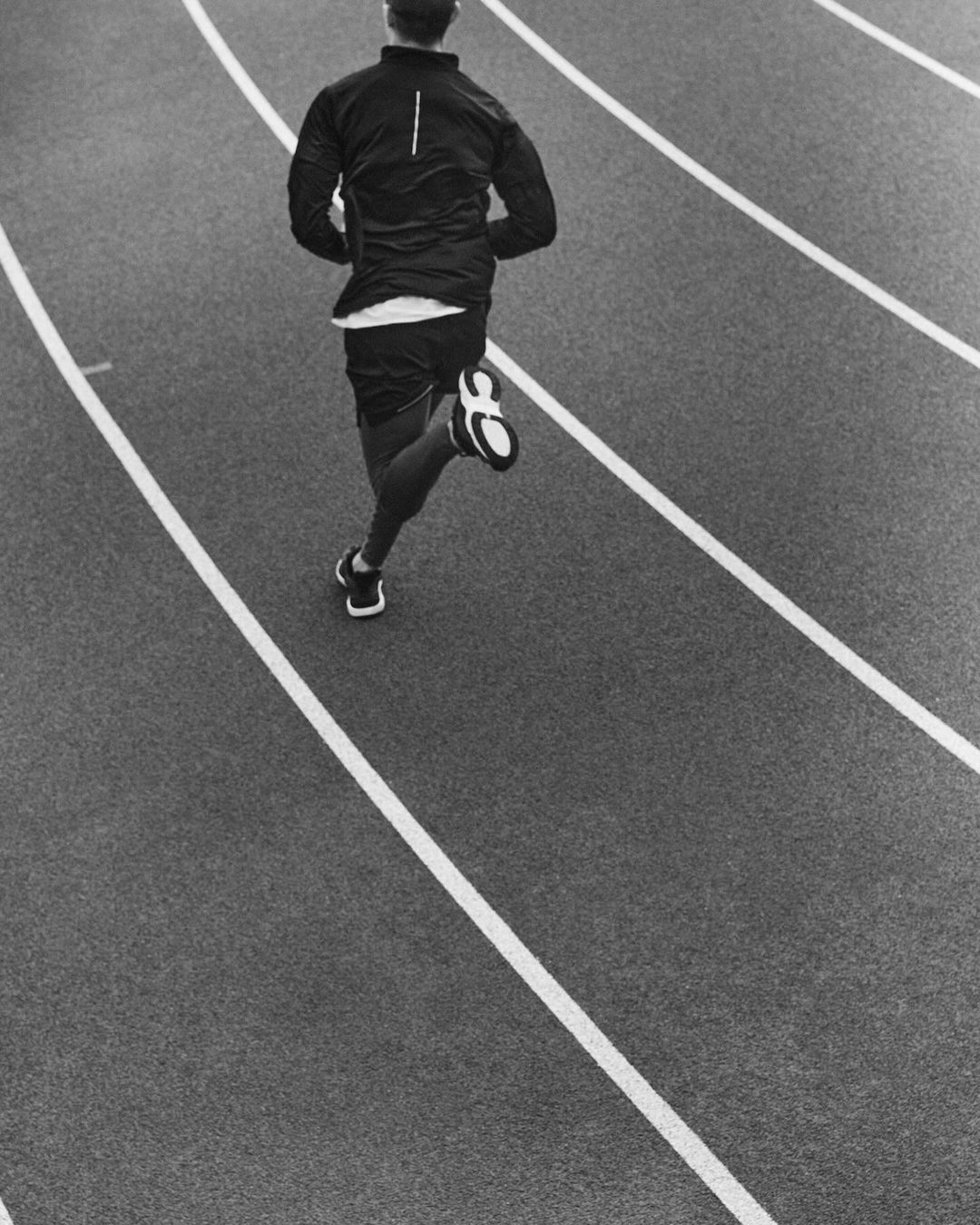 Monochrome shot from above of a man in sportswear running on a track with white lane markings, showcasing athletic activity and training.