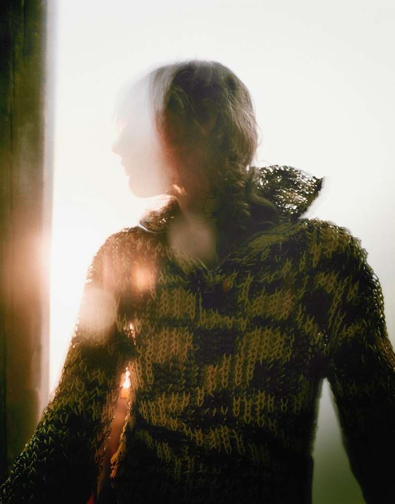 Blurred silhouette of a person wearing a brown knitted sweater. Warm lighting highlights the texture of the garment.