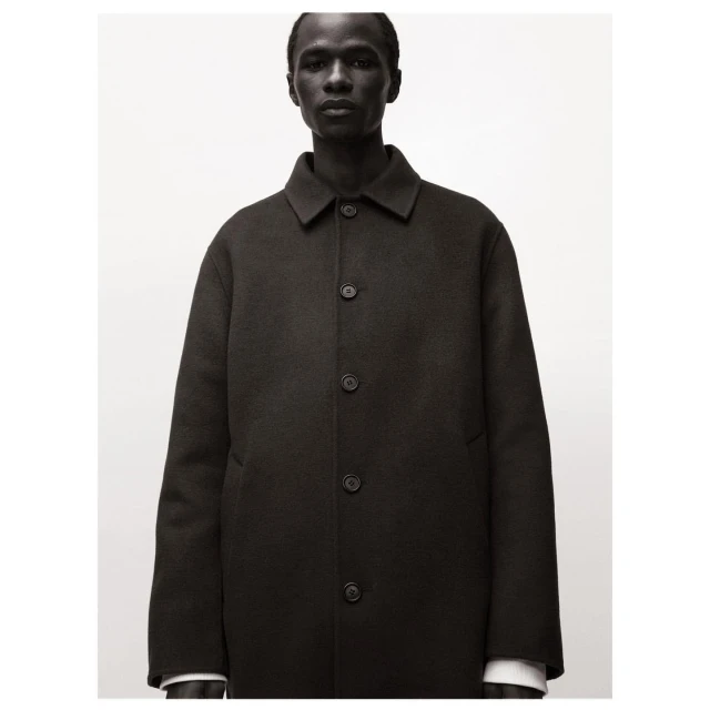 Headshot of a dark-skinned male model in a buttoned black wool overcoat against a neutral background in studio lighting.