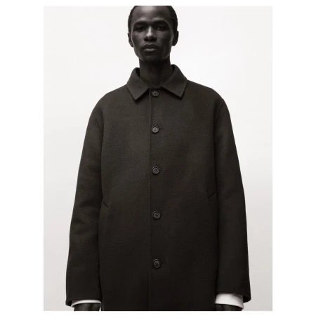 Headshot of a dark-skinned male model in a buttoned black wool overcoat against a neutral background in studio lighting.