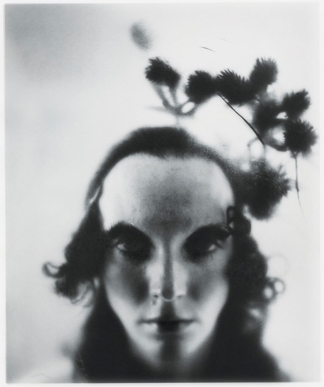 Monochromatic close-up of a person's face with dark hair and striking features, adorned with a delicate floral headpiece against a soft background.