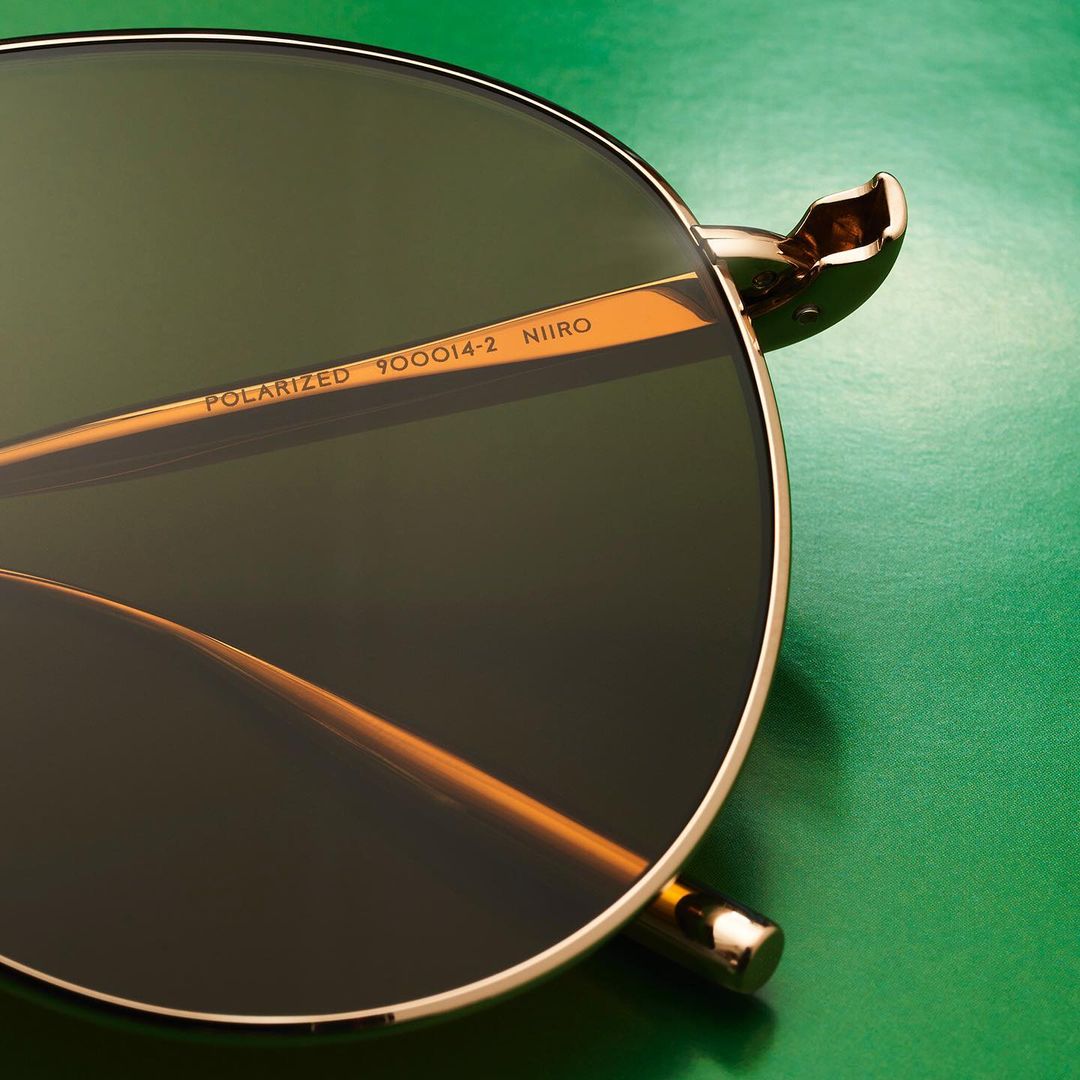 Closeup of polarized sunglasses with gold frames and green lenses against a vibrant green background, featuring 'Niioro' text.