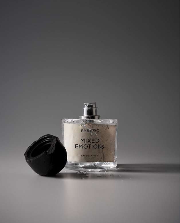 Byredo Mixed Emotions fragrance: clear glass bottle with black cap on gray surface. Modern beauty product shot. Cosmetic still life.