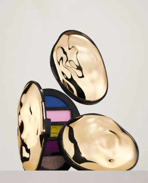 Still life shot of three makeup eyeshadow palettes with reflective gold lids against a neutral background in a minimalist composition.