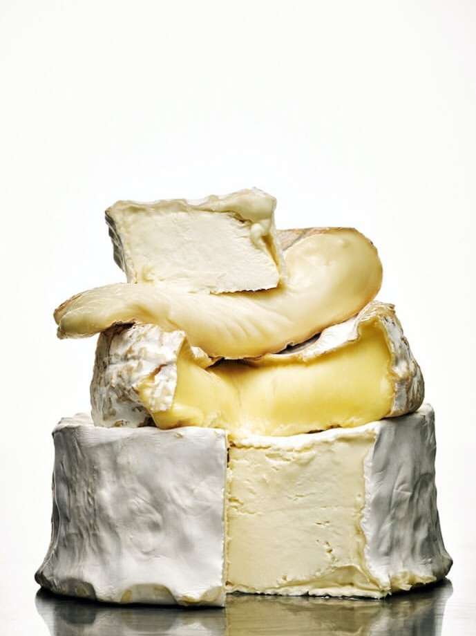 Stack of different cheeses including camembert, brie, and goat cheese against a white backdrop. Dairy food photography.