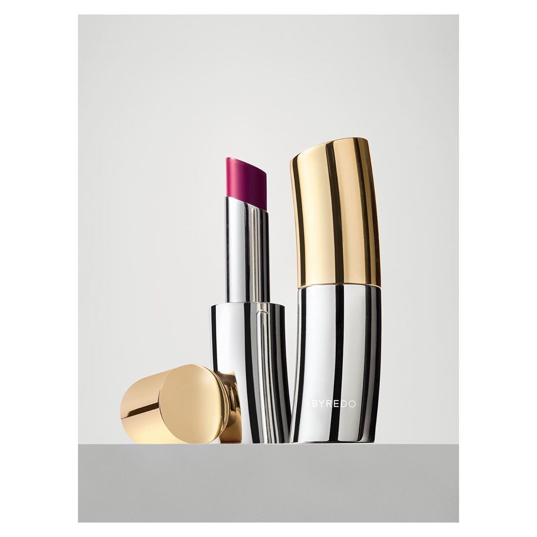 Silver and gold lipstick tubes with one open showing the purple color, displayed on a white surface against a white backdrop.