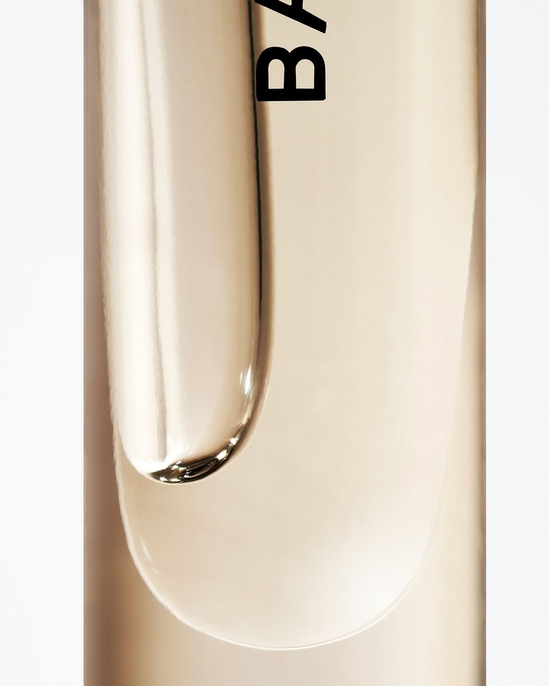 Close-up studio shot of clear beauty serum with label detail against a white background, highlighting product texture and branding.