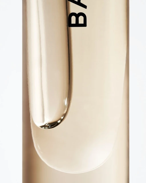 Close-up studio shot of clear beauty serum with label detail against a white background, highlighting product texture and branding.