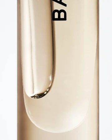 Close-up studio shot of clear beauty serum with label detail against a white background, highlighting product texture and branding.