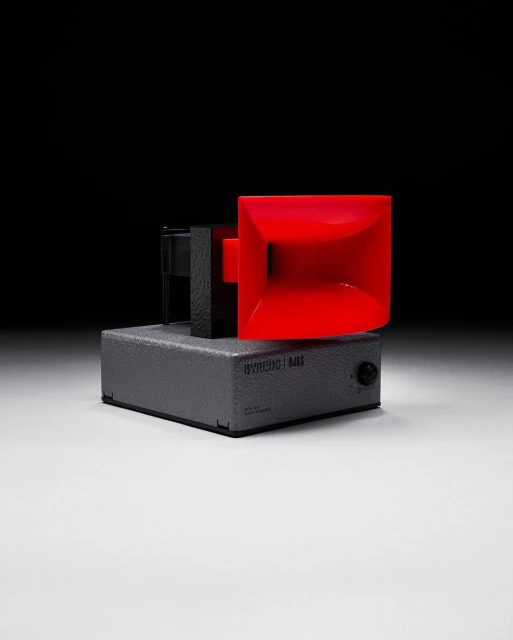 Red and black electronic device on a gray base against a dark background, product shot for music or technology industries.