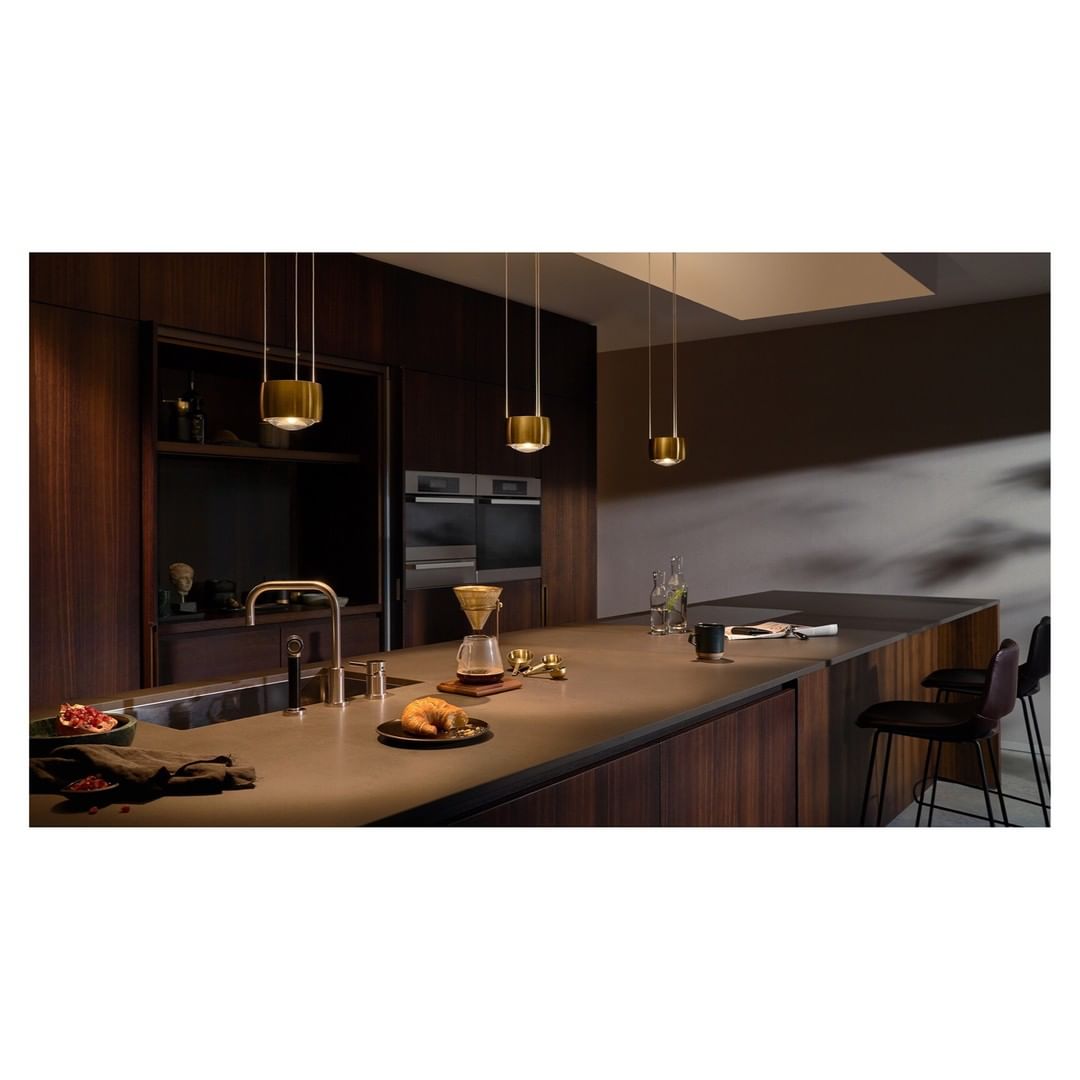 Contemporary kitchen interior with a dark wood island, brass pendant lights, and modern appliances creating a stylish and functional space.