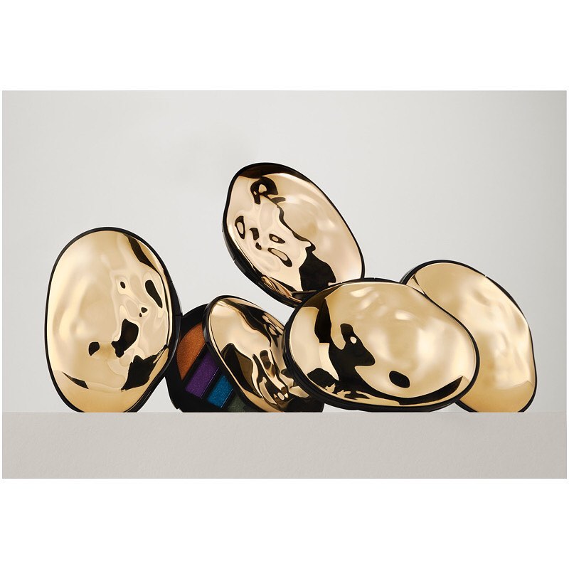Eye-catching beauty shot of makeup palette nestled among golden, organic-shaped cosmetic containers on a sleek white surface.