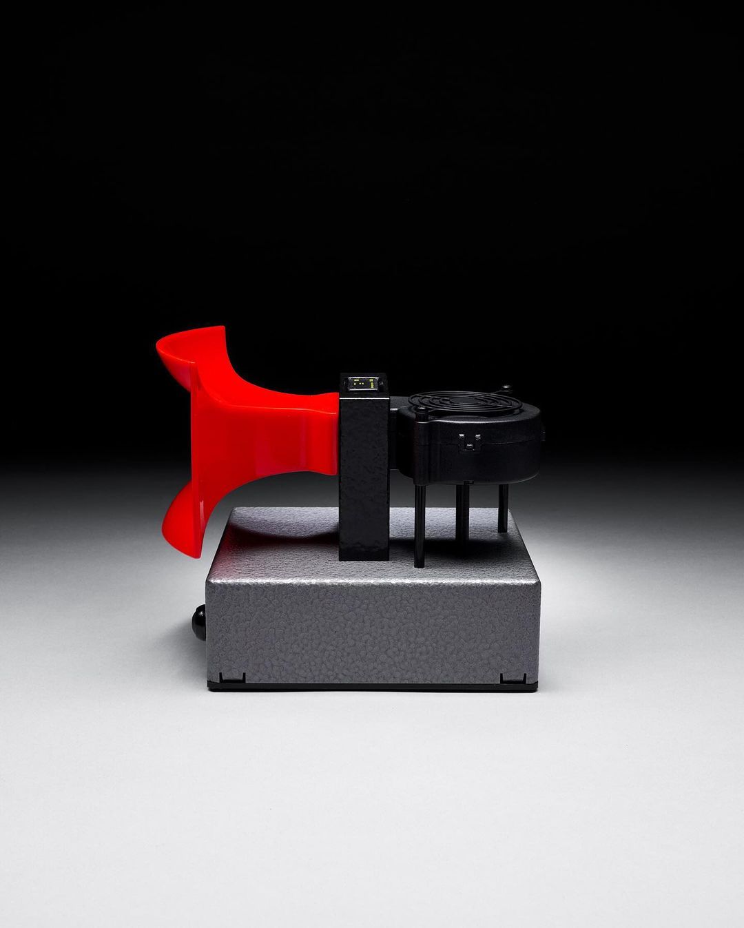 Macro shot of a red and black industrial switch mechanism on a gray metal box against a dark background, product photography.