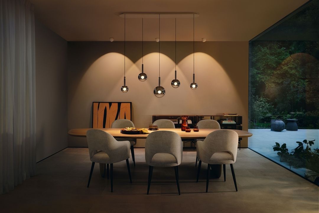 Dining room interior with a wooden table, six chairs, and pendant lights, featuring a modern design and neutral color palette.