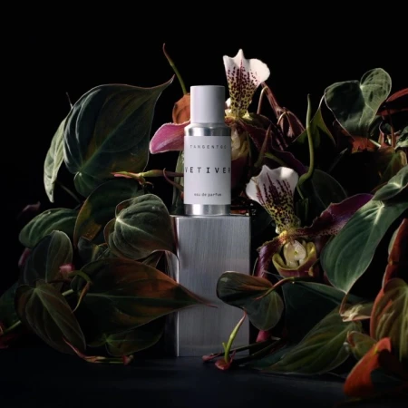 Perfume bottle by Tangent GC, 'Vetiver' scent, centered on a metallic block surrounded by green foliage and exotic orchid flowers, studio lit.