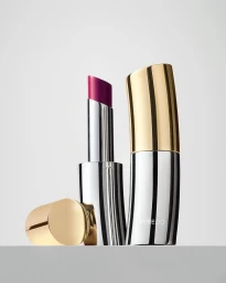 Byredo lipstick with polished silver and gold curved case next to a separated gold cap against a light background
