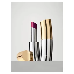 Byredo lipstick in a curved metallic silver and gold case with a bright magenta bullet against grey