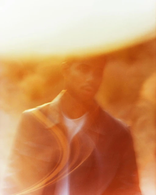 Portrait of a man in a jacket with blurred effects in a golden-toned light. The image features soft focus and a dreamy atmosphere.