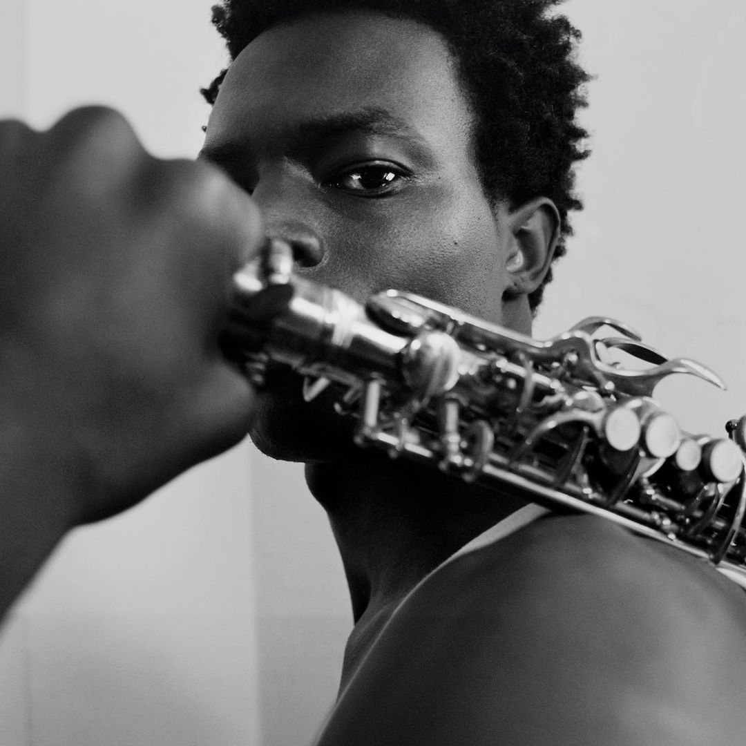 Black and white close-up portrait of an adult male holding a saxophone, featuring detailed focus on the instrument and his face.