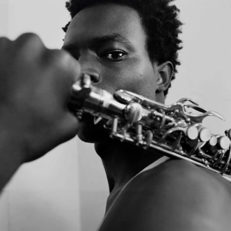 Black and white close-up portrait of an adult male holding a saxophone, featuring detailed focus on the instrument and his face.