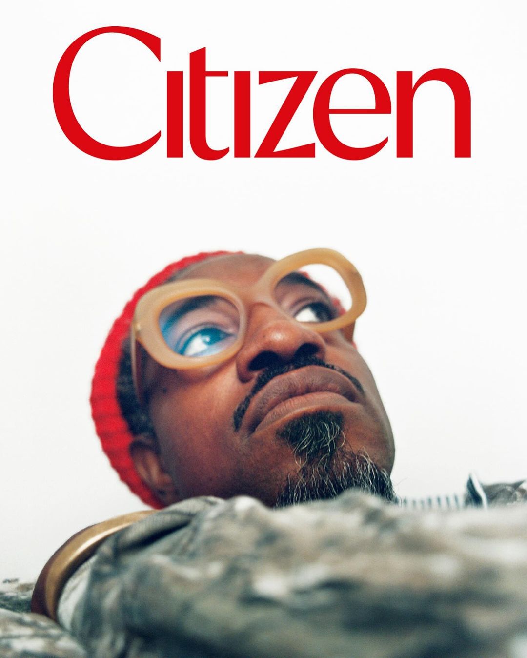 Close-up studio shot of African-American adult male wearing stylish glasses and red beanie, looking up with 'Citizen' text visible.