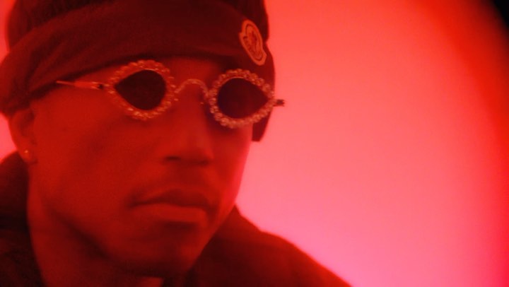 Close-up of a person wearing beaded glasses and a headband, bathed in red lighting, creating a striking and artistic portrait.