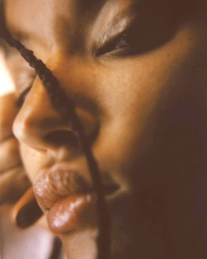 Close-up on an adult female face with tan skin, one eye visible, partial view of nose, lips, and hand holding a dark braided strand.