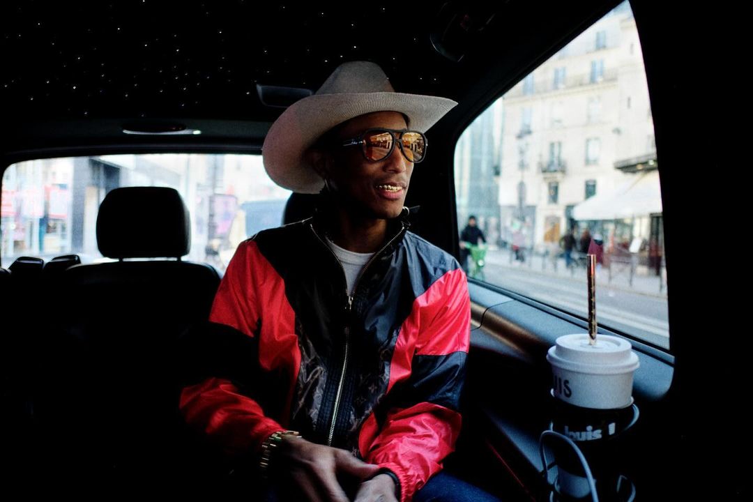 Adult male wearing a cowboy hat and jacket in a car, city buildings visible in background through the window, daytime.