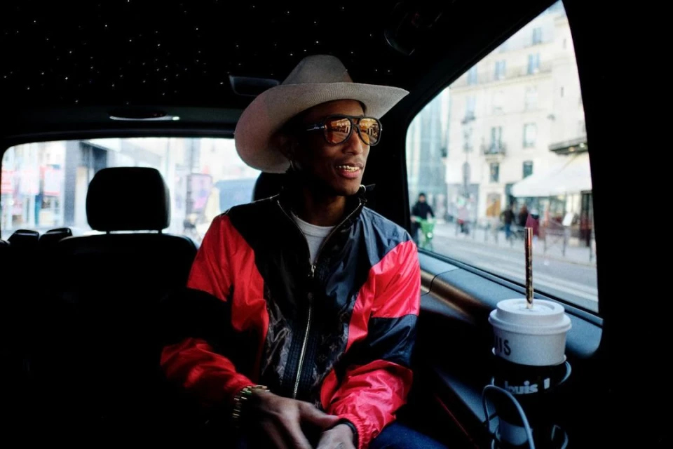 Adult male wearing a cowboy hat and jacket in a car, city buildings visible in background through the window, daytime.