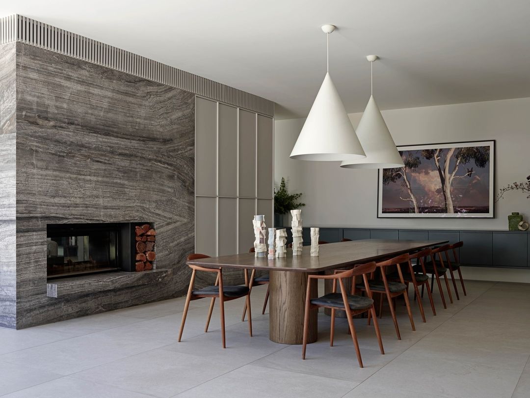 Modern dining room interior with a wooden table, black chairs, cone-shaped pendant lights, and a marble fireplace. Interior design.