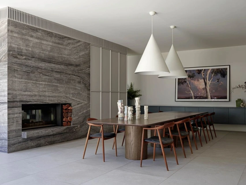 Modern dining room interior with a wooden table, black chairs, cone-shaped pendant lights, and a marble fireplace. Interior design.