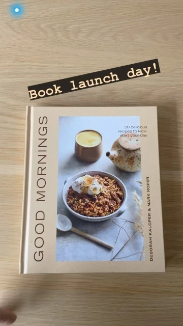 Close-up shot of a cookbook titled 'Good Mornings' with a food photography displayed on the cover, set on a wooden surface.