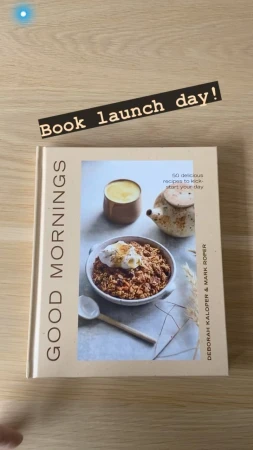 Close-up shot of a cookbook titled 'Good Mornings' with a food photography displayed on the cover, set on a wooden surface.