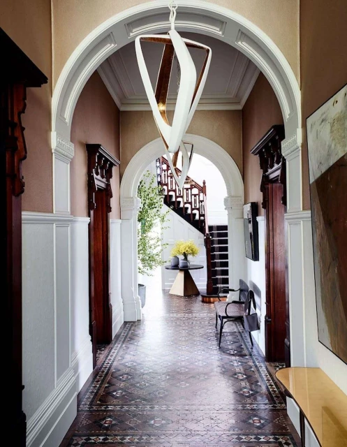 Interior view of a hallway featuring a modern geometric pendant light, an arched doorway, and a patterned tile floor in a residential building.