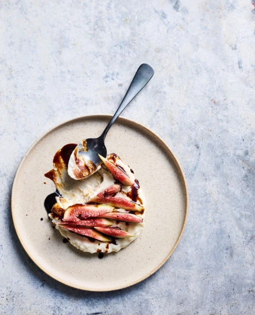 Overhead shot of a fig and cream cheese dessert drizzled with sauce on a tan plate, presented on a mottled gray background.