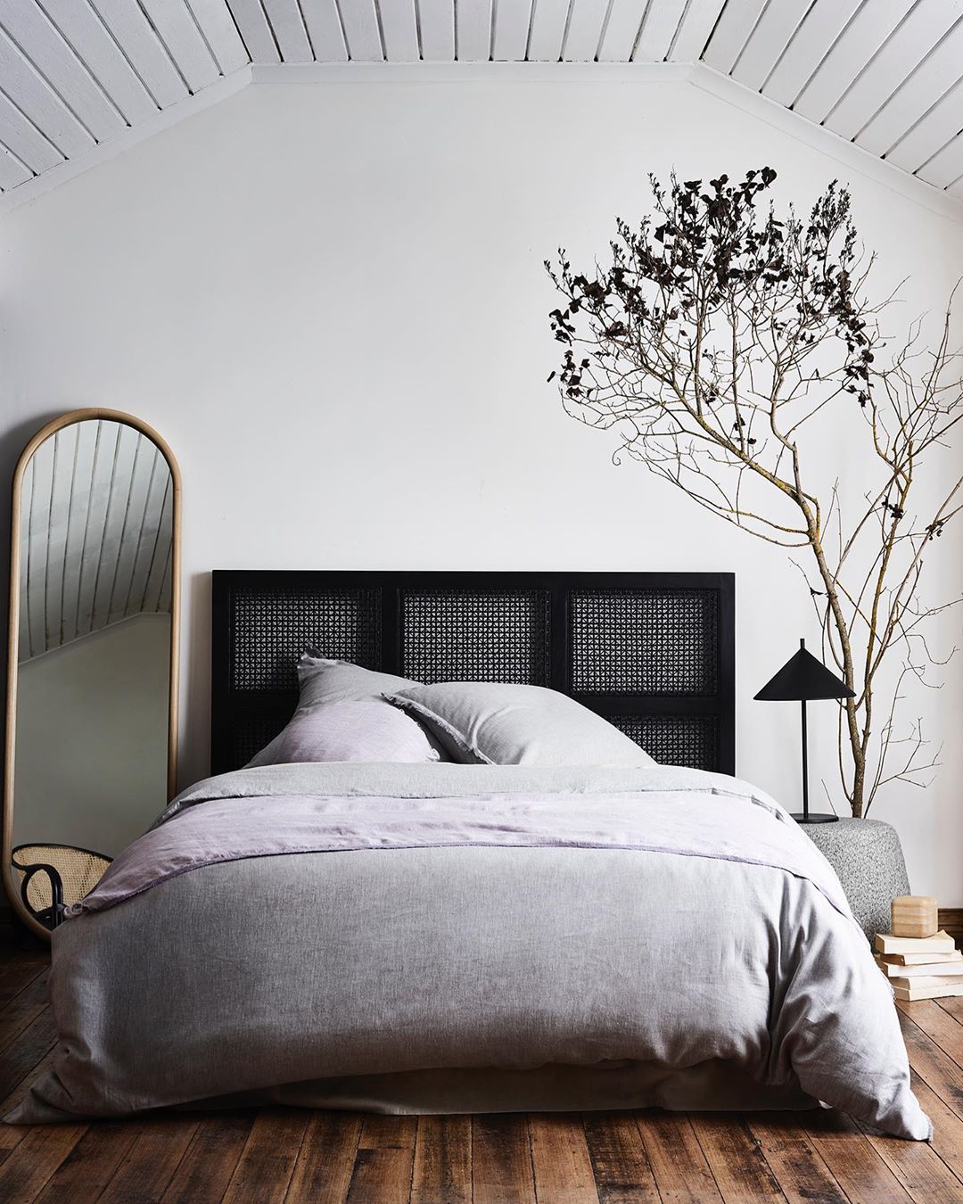 Bedroom interior with a black headboard, grey bedding, and a minimalist tree in a pot, creating a serene and modern aesthetic.
