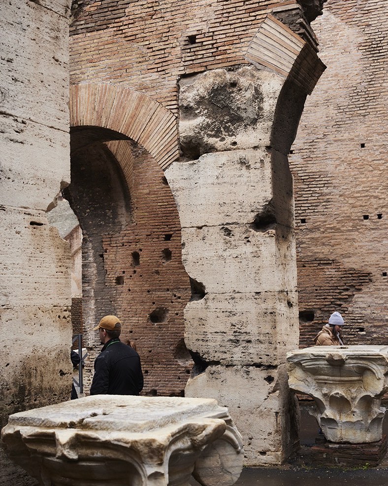 Interior view of the Colosseum in Rome featuring brick and stone walls with archways, and a couple of people in the background.