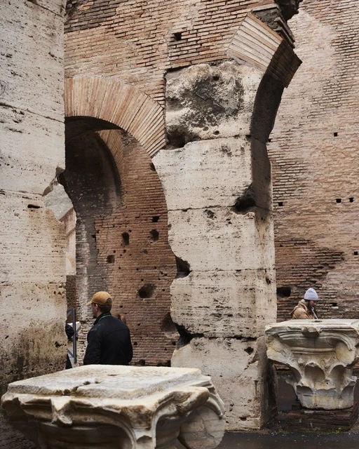 Interior view of the Colosseum in Rome featuring brick and stone walls with archways, and a couple of people in the background.
