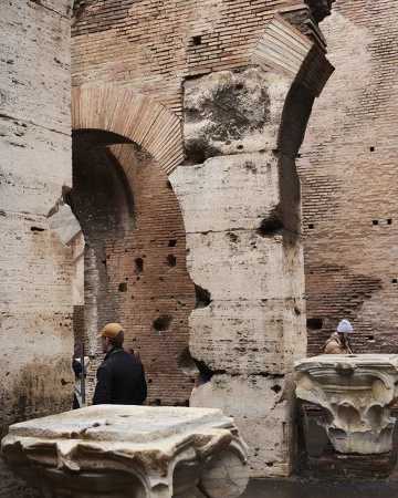 Interior view of the Colosseum in Rome featuring brick and stone walls with archways, and a couple of people in the background.