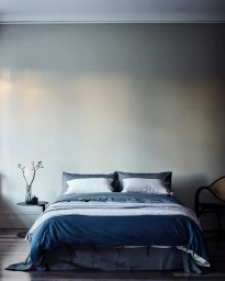 A made bed with blue and grey linens against a solid grey wall, captured by photographer Mark Roper.