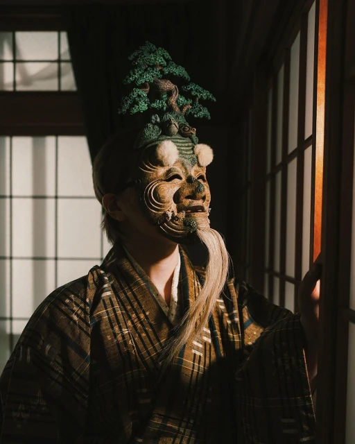 Person in traditional Japanese attire with elaborate mask and headdress standing near a window with natural light casting soft shadows.