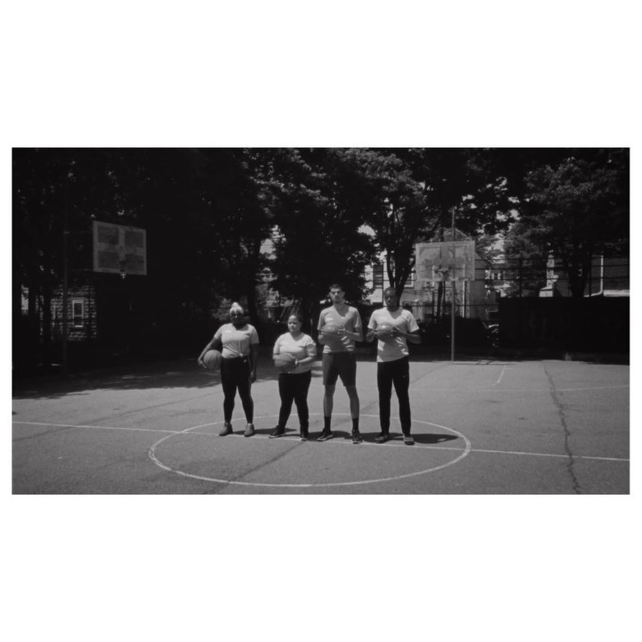 Four people stand on a basketball court in a black and white photo, each holding a basketball, with trees and buildings visible behind them.