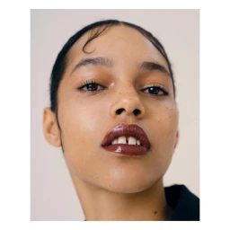 Close-up portrait of a woman with glossy dark lips and dark hair against a plain light background directed by Bon Duke.