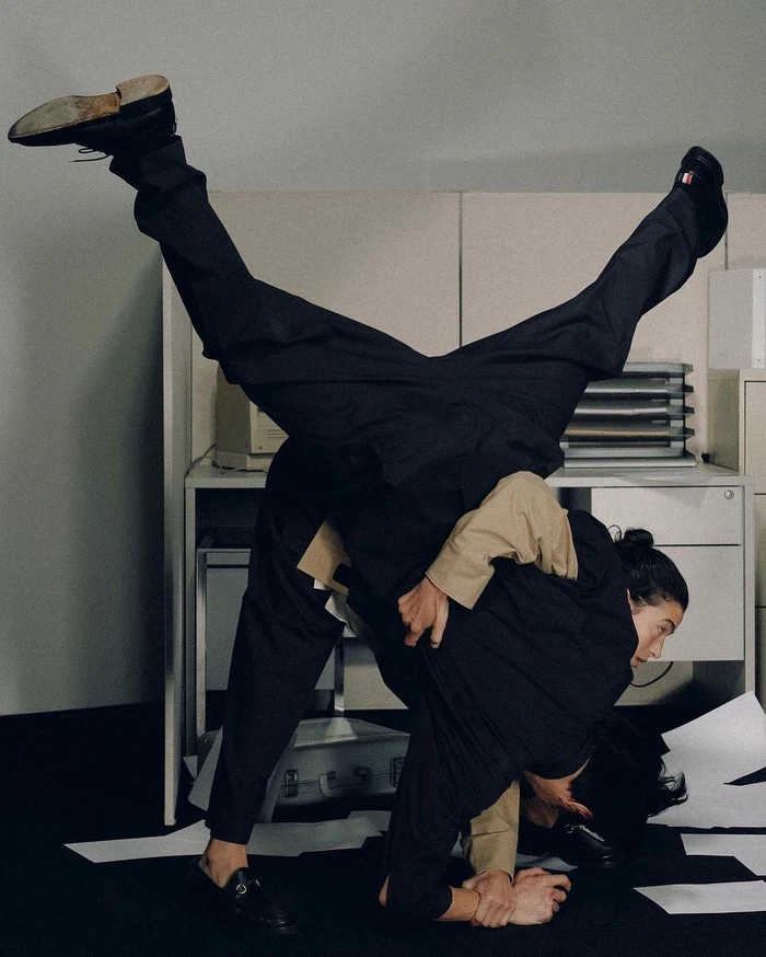 Two people grappling and tumbling upside down in an office setting surrounded by scattered papers