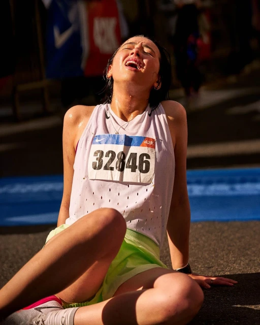 Exhausted female marathon runner sitting on ground, catching her breath after the race. She is wearing a race bib number 32846.