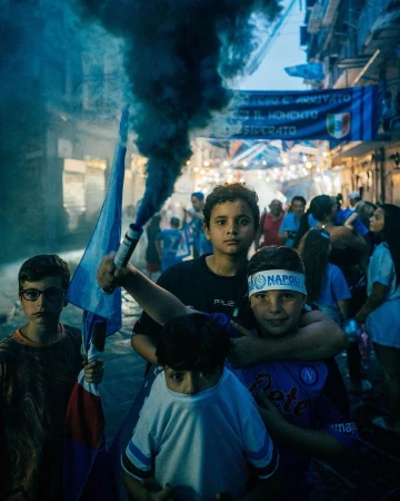 A group of children with flags and a smoke grenade in a city street, expressing support for the Napoli soccer club, with a banner visible.