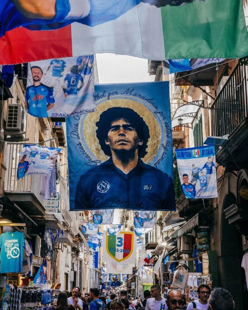 Street in Naples, Italy decorated with flags and banners, including a large banner with an image of soccer player Diego Maradona.